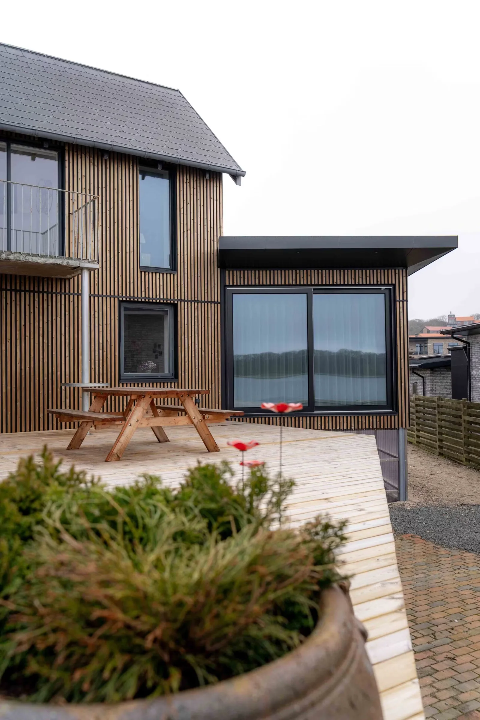 Two-story home clad in warm brown Aluwood slats with a picnic table on the front deck.