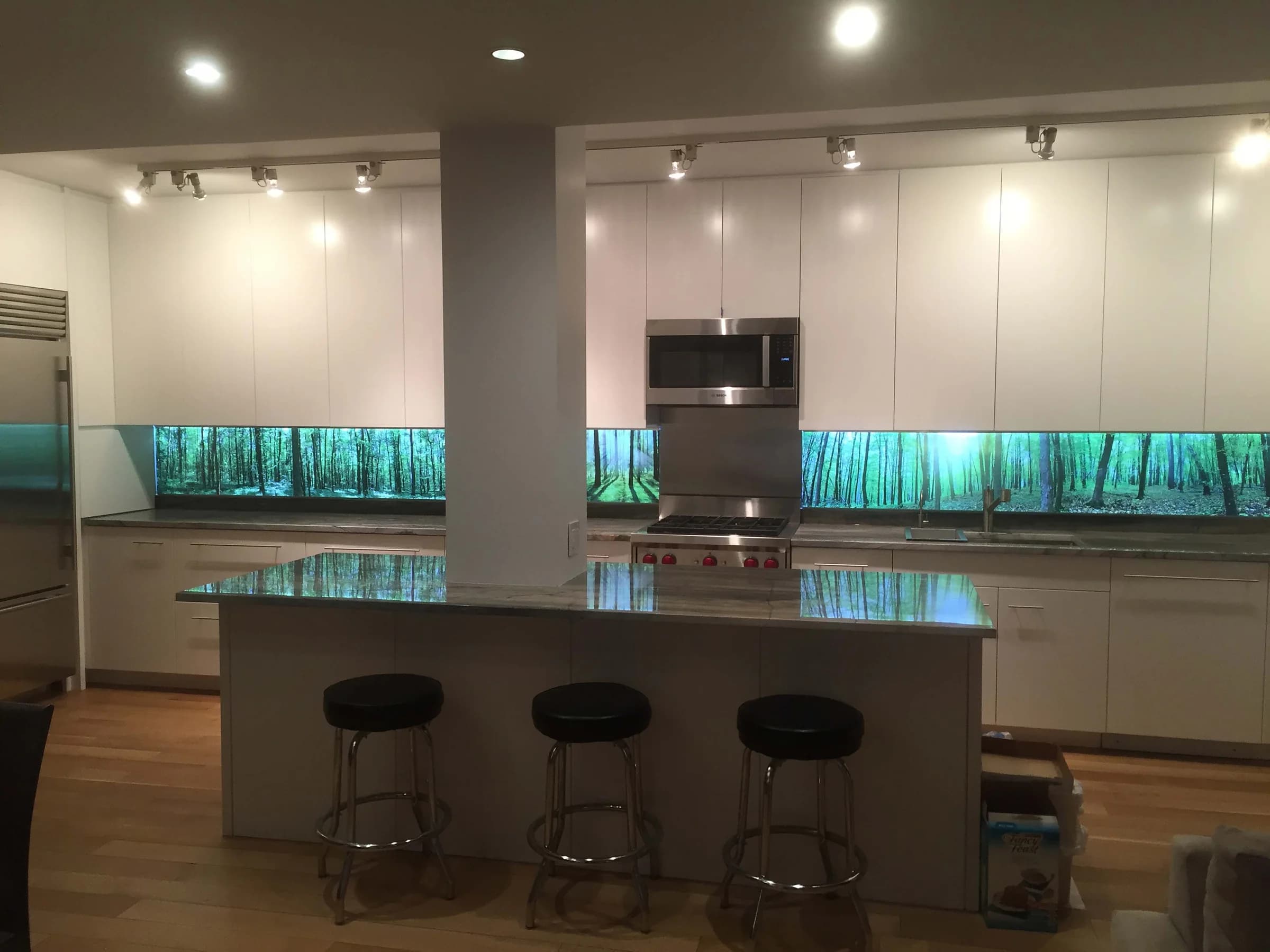 Kitchen island and backsplash with LumiSplash panels glowing blue-green under a forest image.