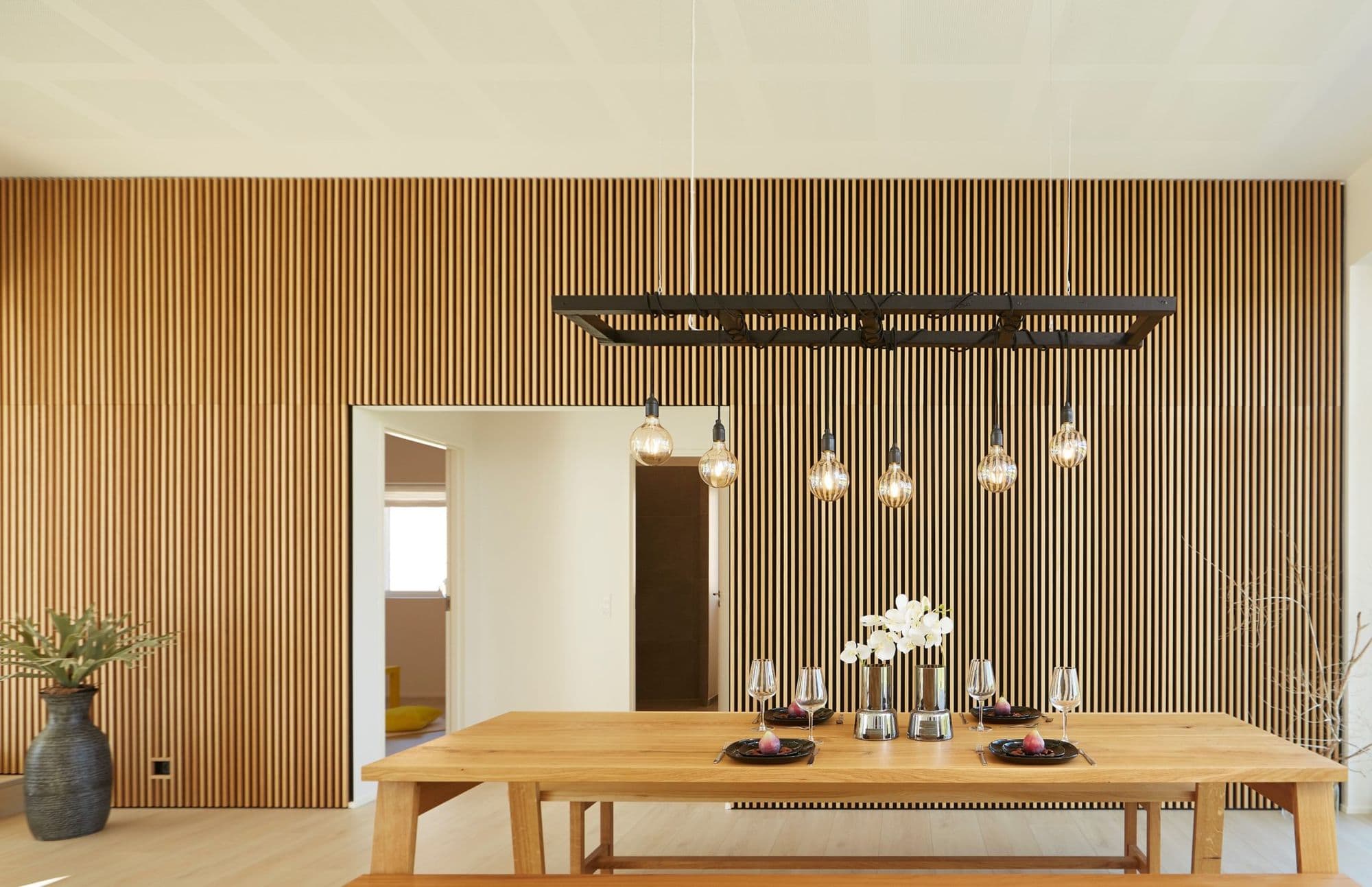 Akupanel oak veneer slats covering a dining room wall around a doorway above a long wooden table.